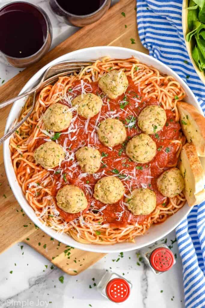 overhead photo of ground chicken meatballs in a bowl with spaghetti and sauce, two pieces of bread sticking out