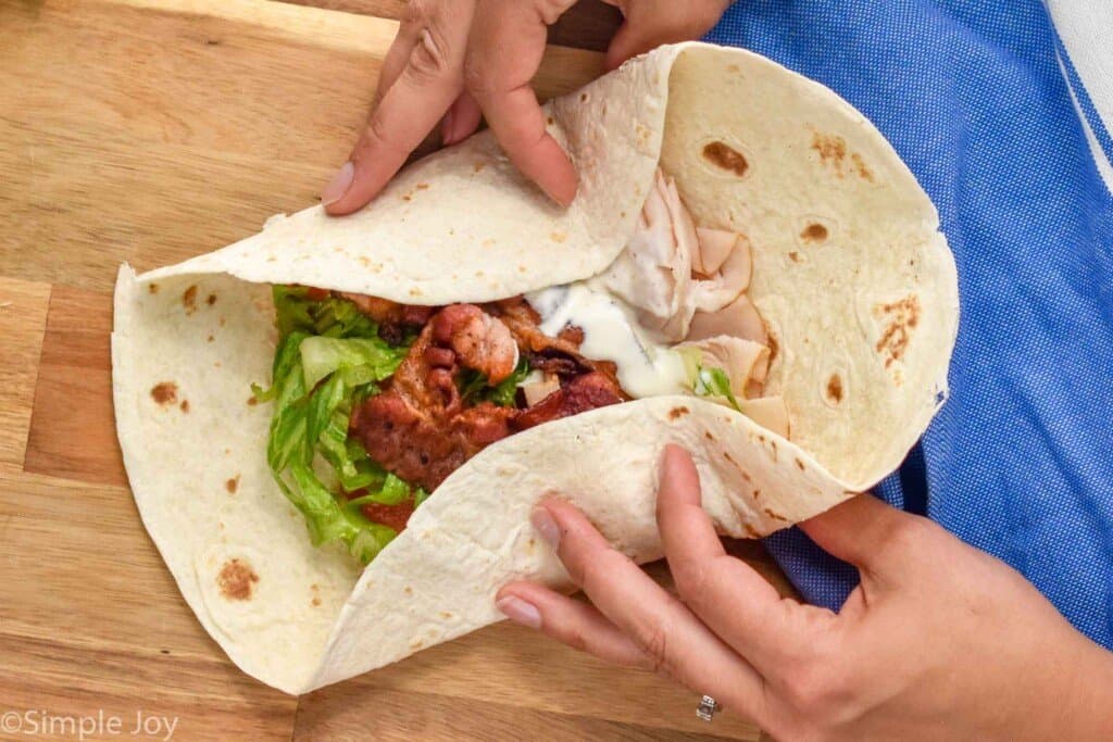 a ranch blt wrap that is being folded in on itself