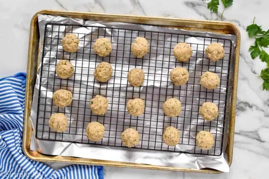 overhead of uncooked chicken parm meatballs on a cooling rack that is in a rimmed baking sheet