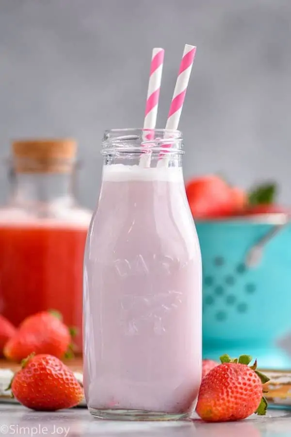 a small milk bottle filled with strawberry milk and two straws