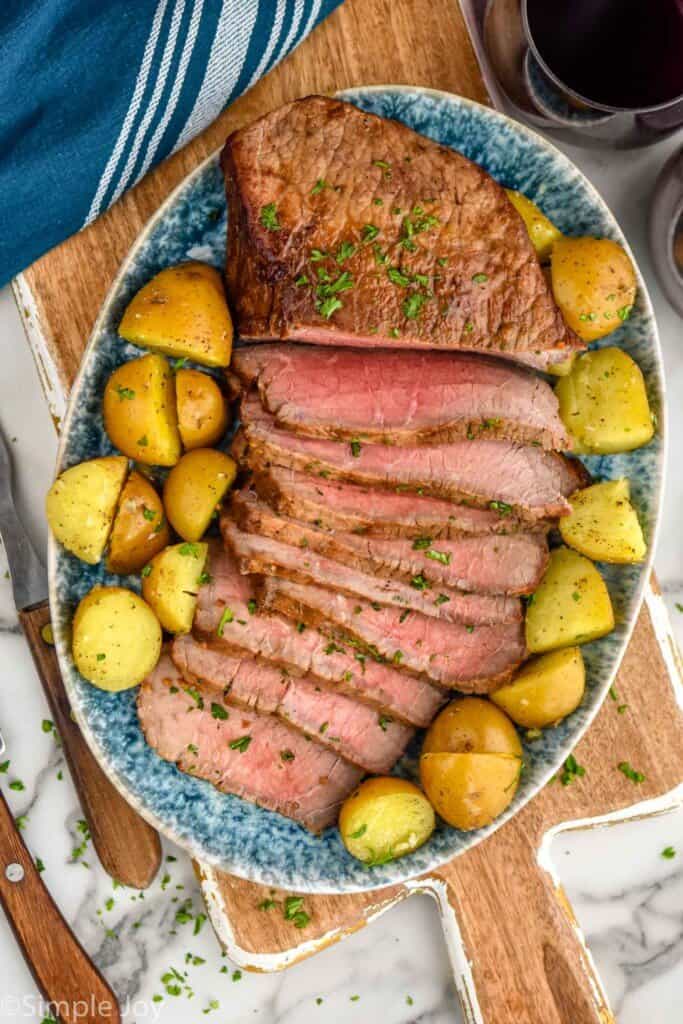 overhead of a London broil recipe cut up on a platter with baby potatoes around it