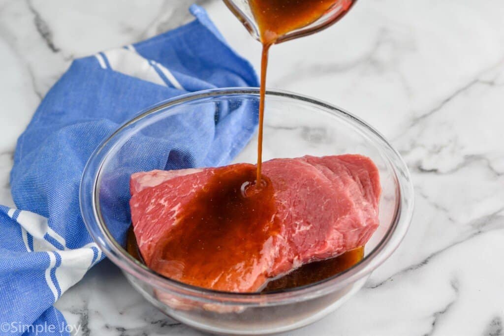London broil marinade being poured over a piece of top round roast
