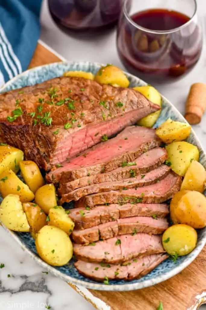 a London broil recipe on a platter, cut up with baby potatoes around it