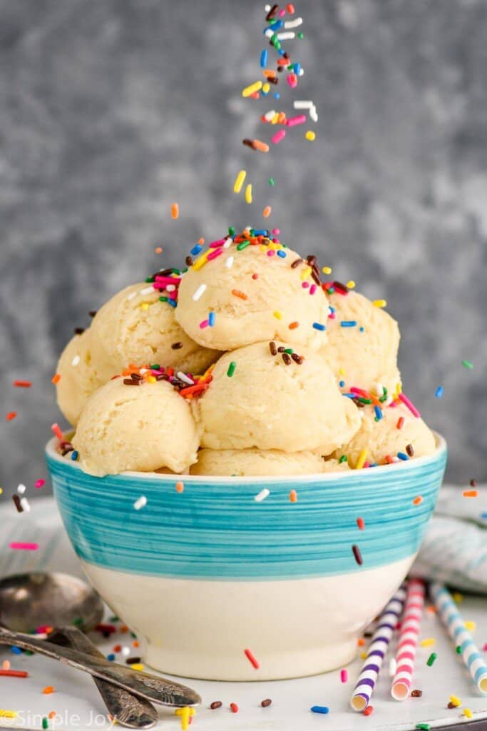 scoops of sugar cookie dough in a bowl with sprinkles being poured on top