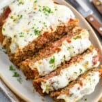 an italian meatloaf sliced and on a serving dish topped with melted cheese and fresh parsley
