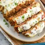 pinterest graphic of an italian meatloaf sliced and on a serving dish topped with melted cheese and fresh parsley