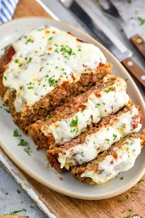 an italian meatloaf sliced and on a serving dish topped with melted cheese and fresh parsley