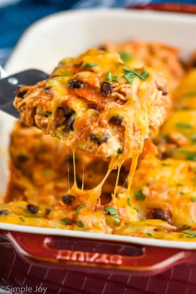 a piece of chicken enchilada casserole being dished out of a baking dish