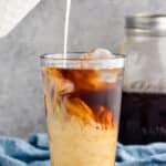 pouring cream into a glass tumbler full of ice and cold brew coffee