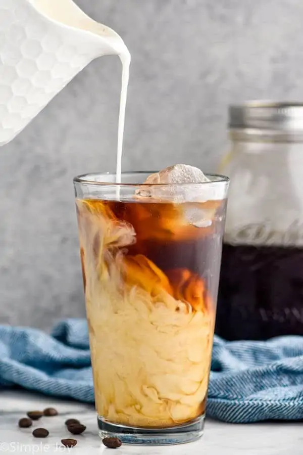 pouring cream into a glass tumbler full of ice and cold brew coffee