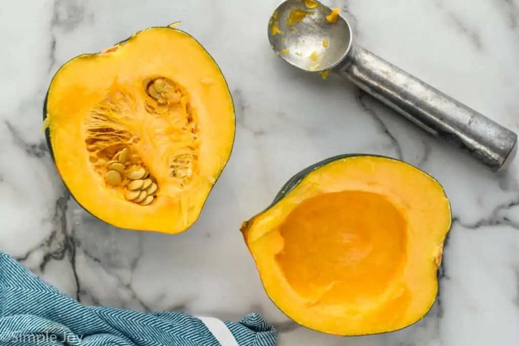 overhead of an acorn squash that has had the seeds removed form one half with an ice cream scooper string next to it