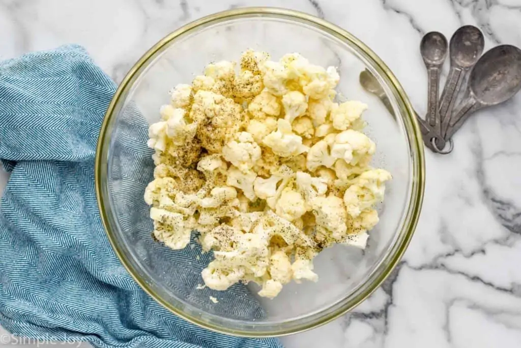 overhead of raw cauliflower florets in a bowl with seasoning