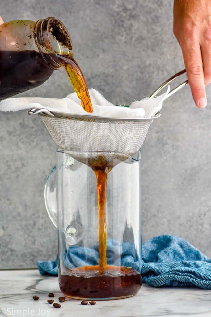 pouring cold brew coffee through a cheese cloth and wire filter into a pitcher