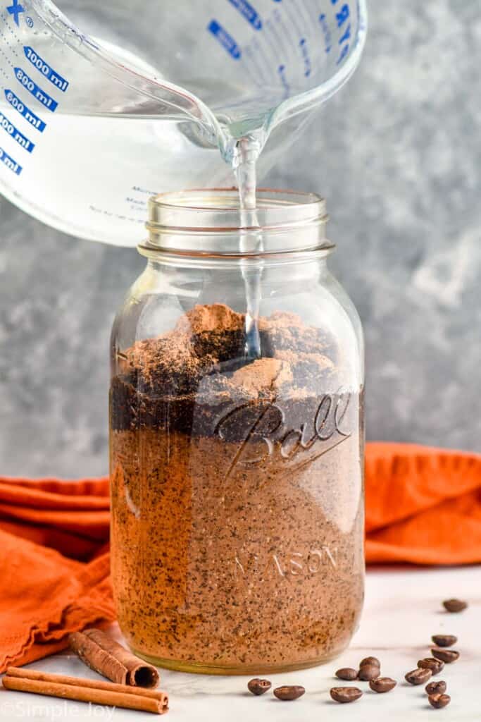 pouring cold water into a mason jar with pumpkin spice and coffee grounds