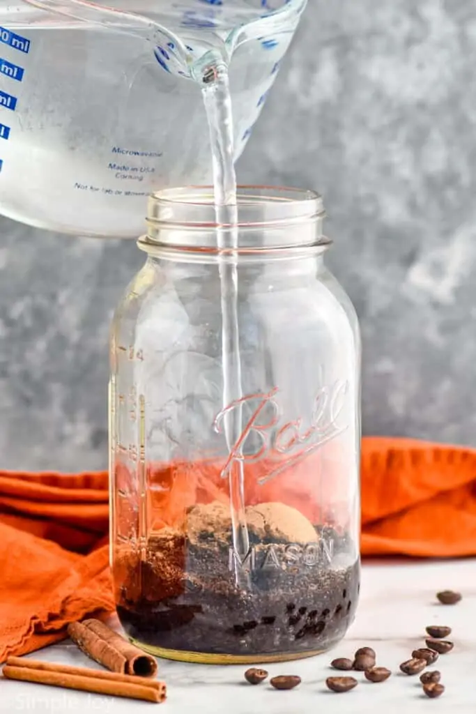 pouring cold water into a mason jar with pumpkin spice and pumpkin spice mix