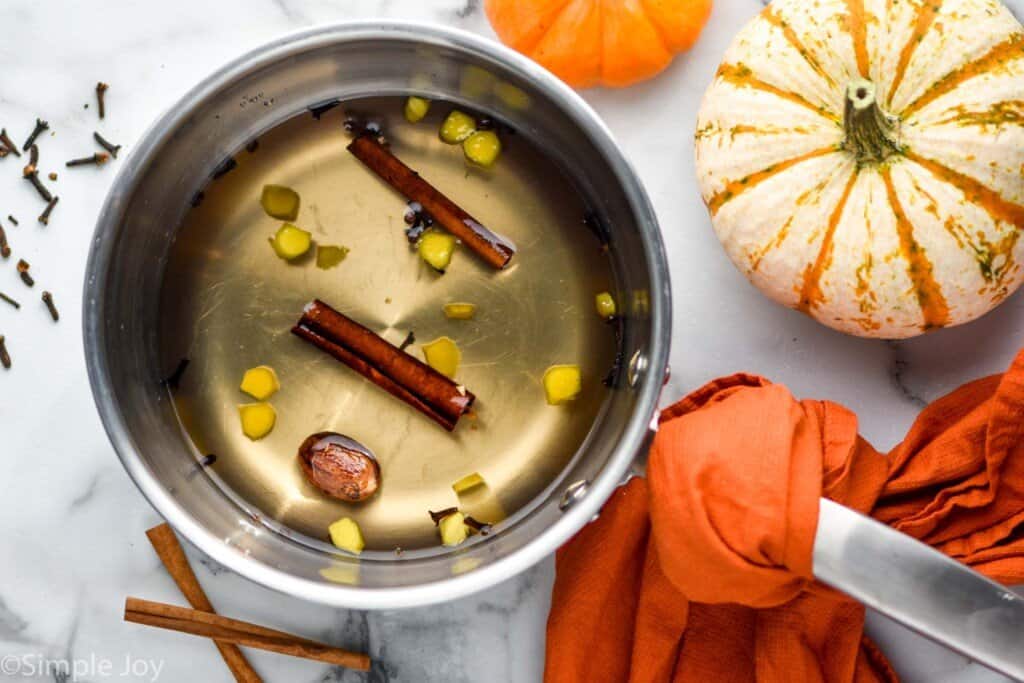 overhead of a pot with syrup, cinnamon sticks, cloves, nutmeg, and ginger to make pumpkin spice syrup