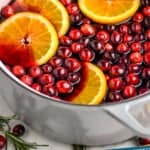 pinterest graphic of side view of hot mulled wine recipe in a stock pot, garnished with fresh cranberries and orange slices