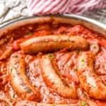 pinterst graphic of side view of italian sausages in sauce with peppers in onions in a skillet