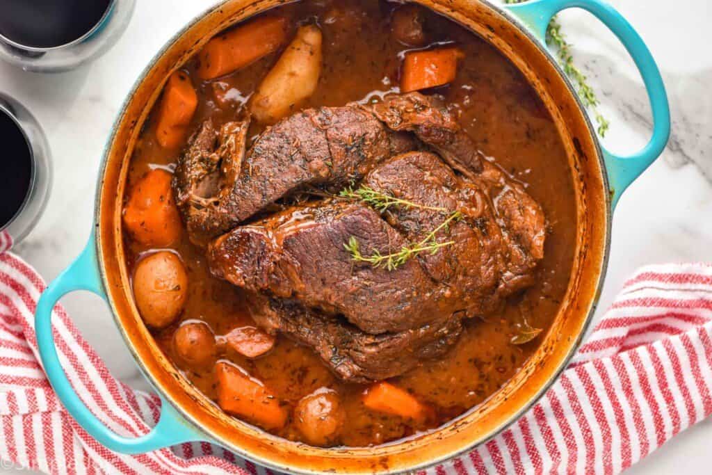 overhead of a pot roast in a dutch oven with vegetables and a thick gravy
