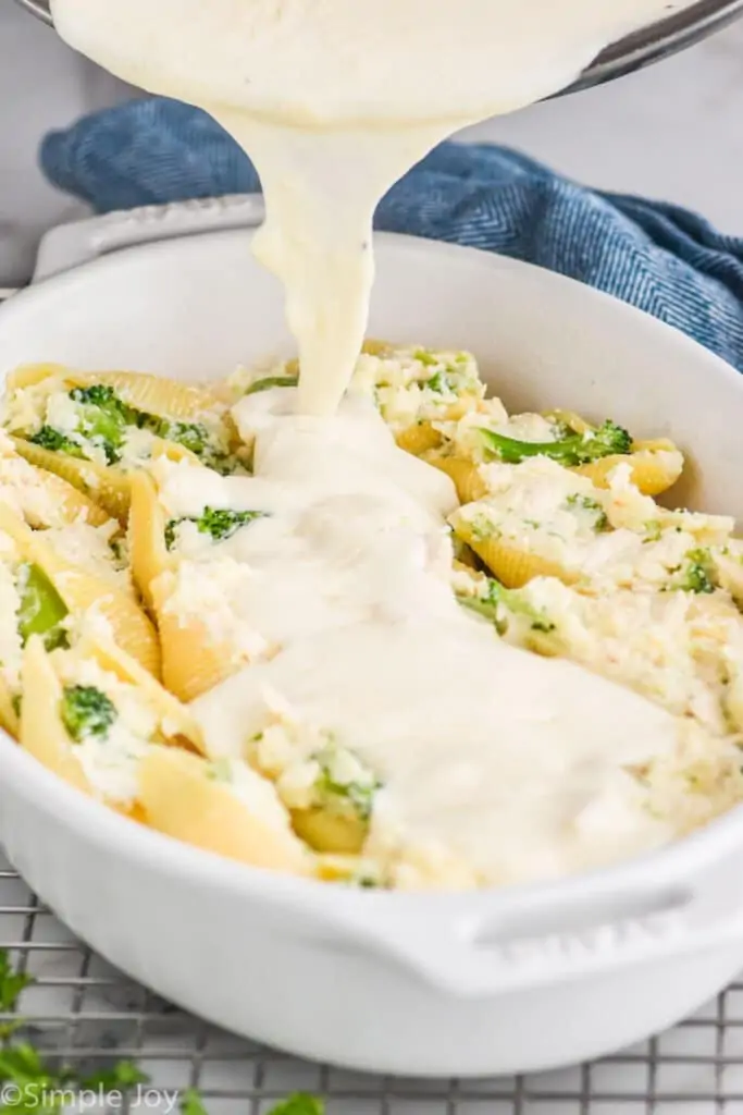 Alfredo Sauce being poured over chicken and broccoli stuffed shells