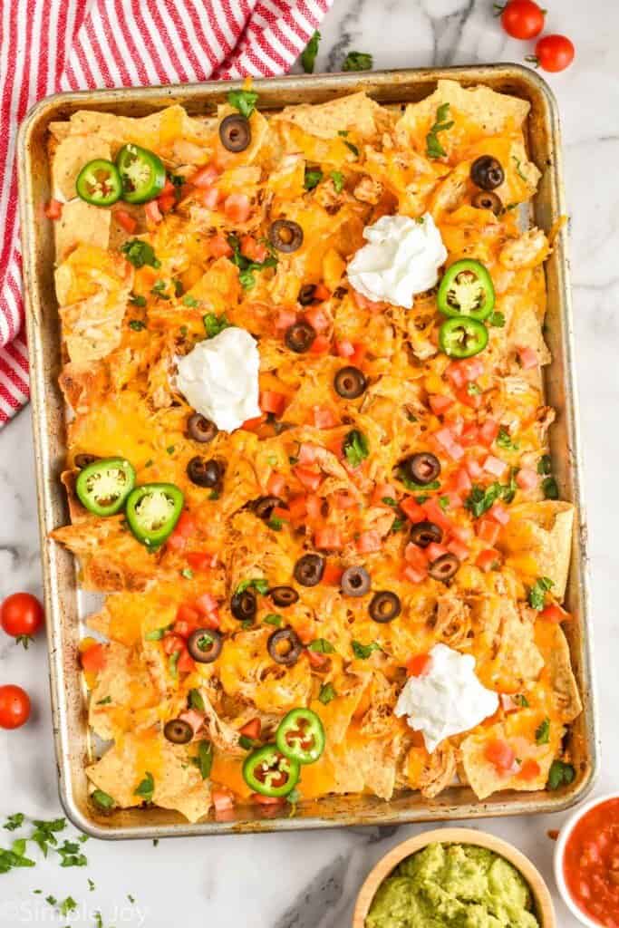 overhead of a chicken nacho recipe topped with olives, sour cream, and sliced jalapeños