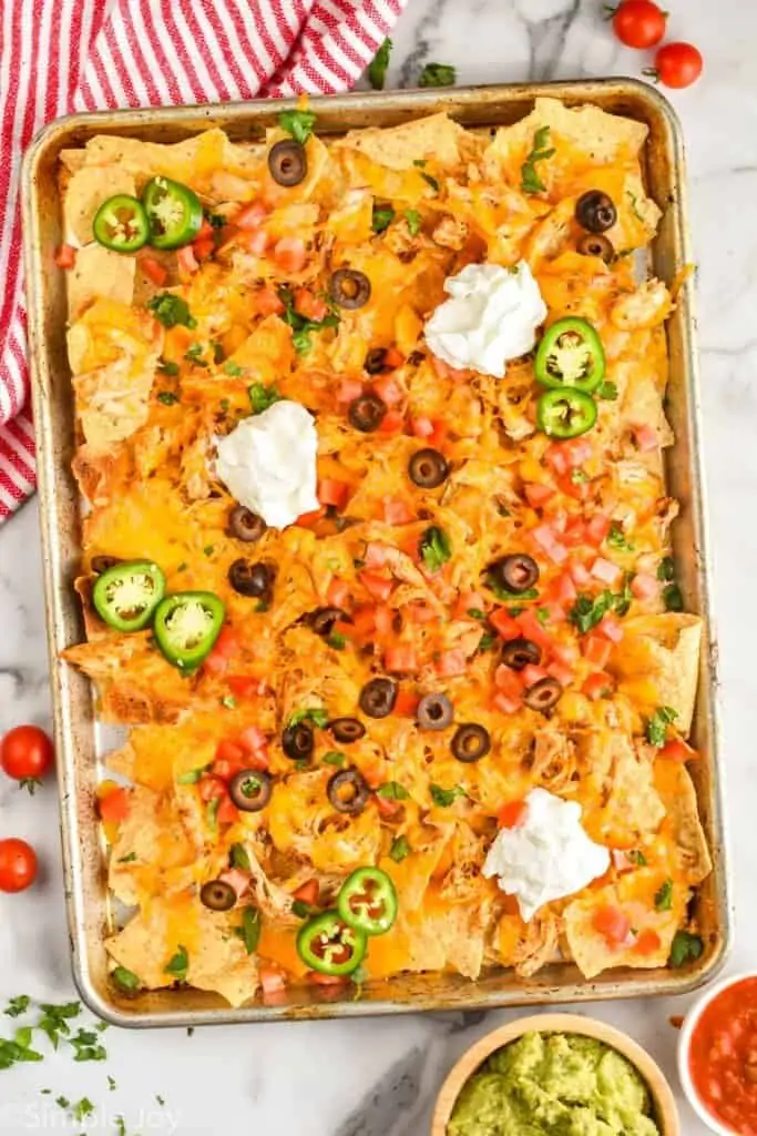 overhead of a chicken nacho recipe topped with olives, sour cream, and sliced jalapeños