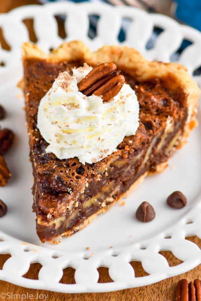 close up of chocolate pecan pie on a white plate topped with whipped cream