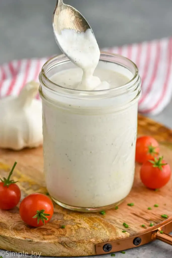 a spoon drizzling creamy garlic dressing into a mason jar