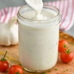 a spoon drizzling creamy garlic dressing into a mason jar