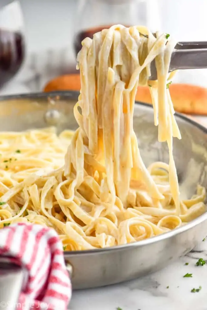 tongs lifting fettuccine alfredo recipe out of a skillet