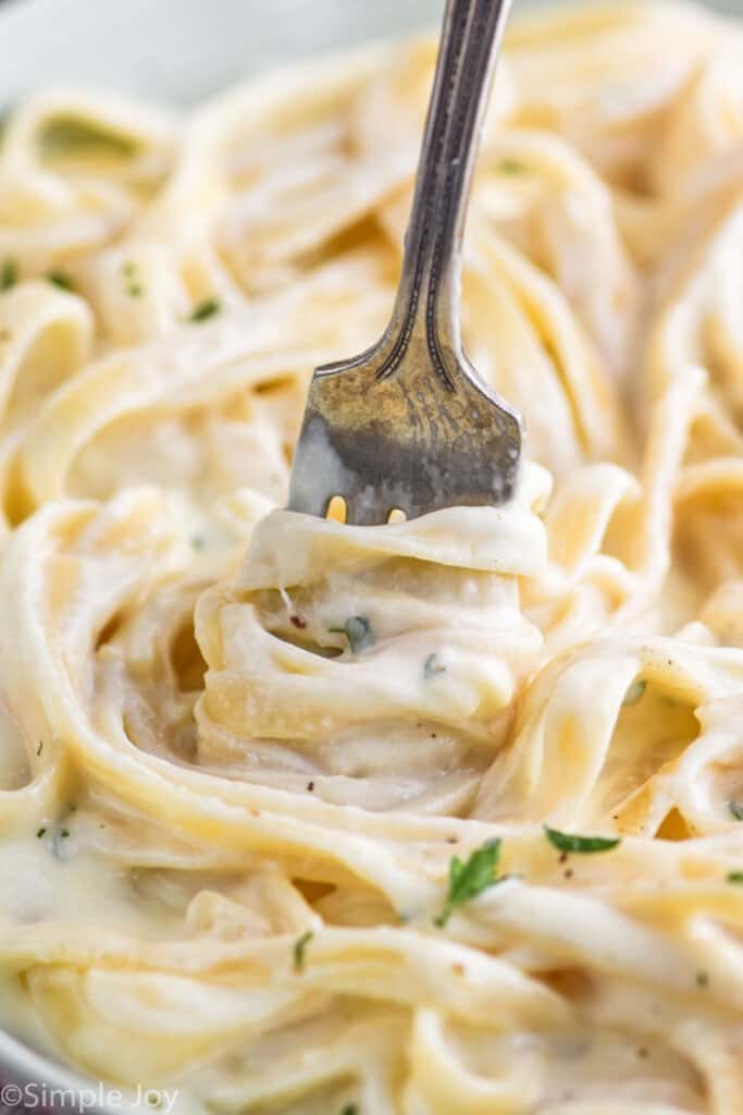 close up of a fork twisting fettuccine noodles covered in alfredo sauce