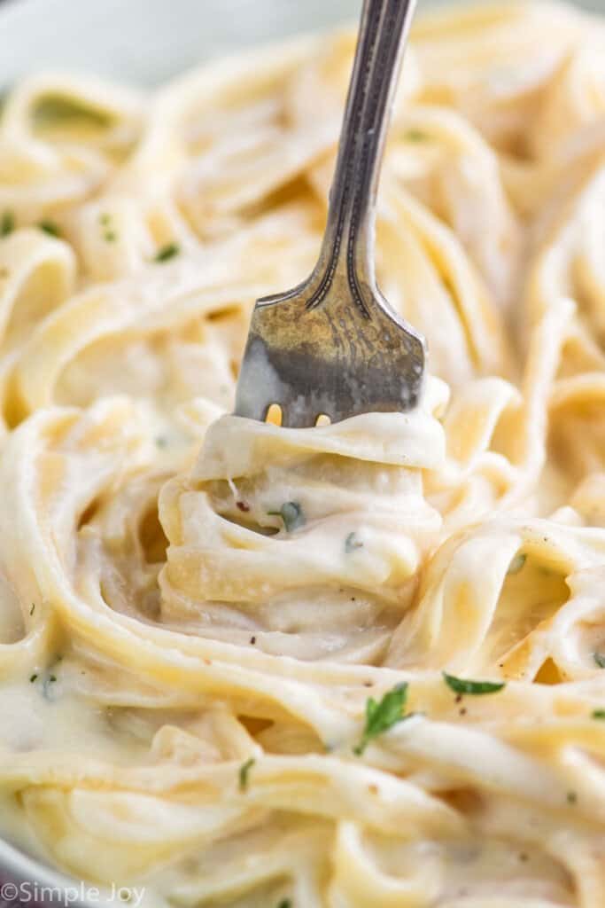 close up of a fork twisting fettuccine noodles covered in alfredo sauce