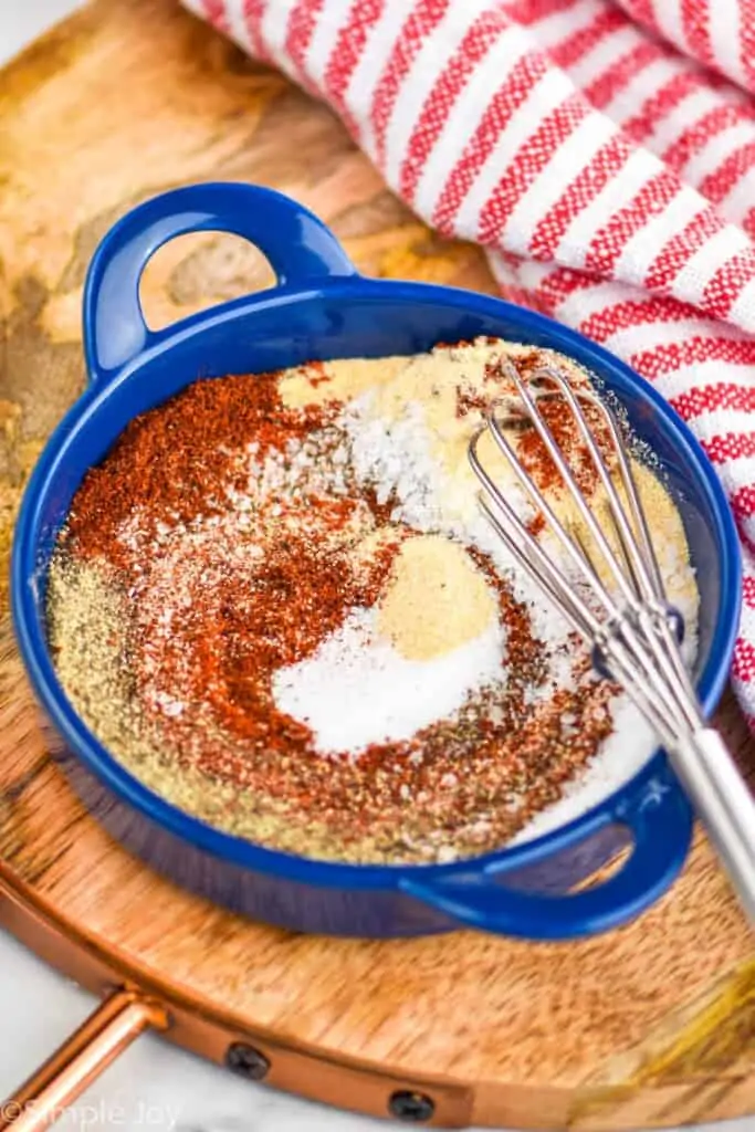 a small blue dish with a small whisk and grill seasoning partially mixed