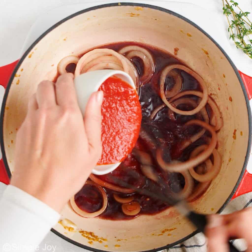 pouring tomato sauce into a dutch oven