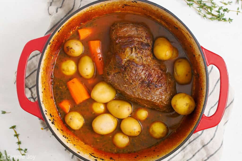 potatoes and carrots being added to a dutch oven with pot roast