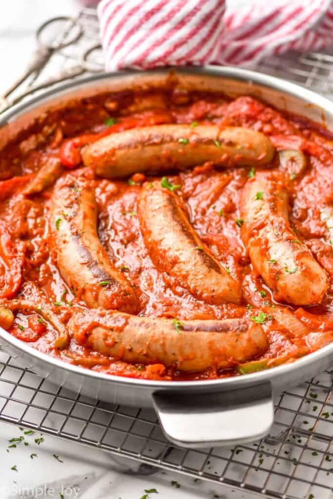 side view of italian sausages in sauce with peppers in onions in a skillet