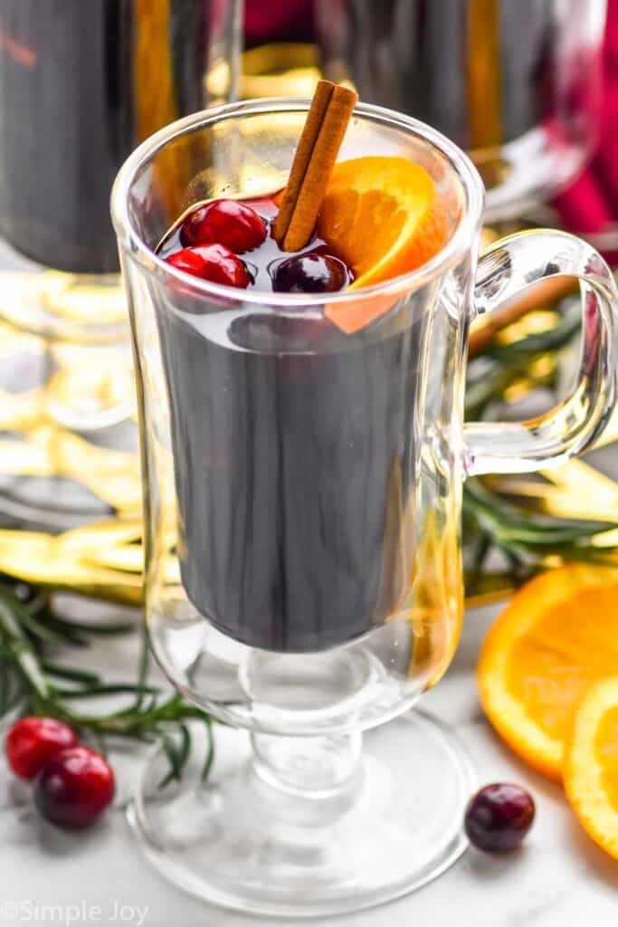 a close up picture of mulled wine in a glass with cranberries and a cinnamon stick and a slice of orange