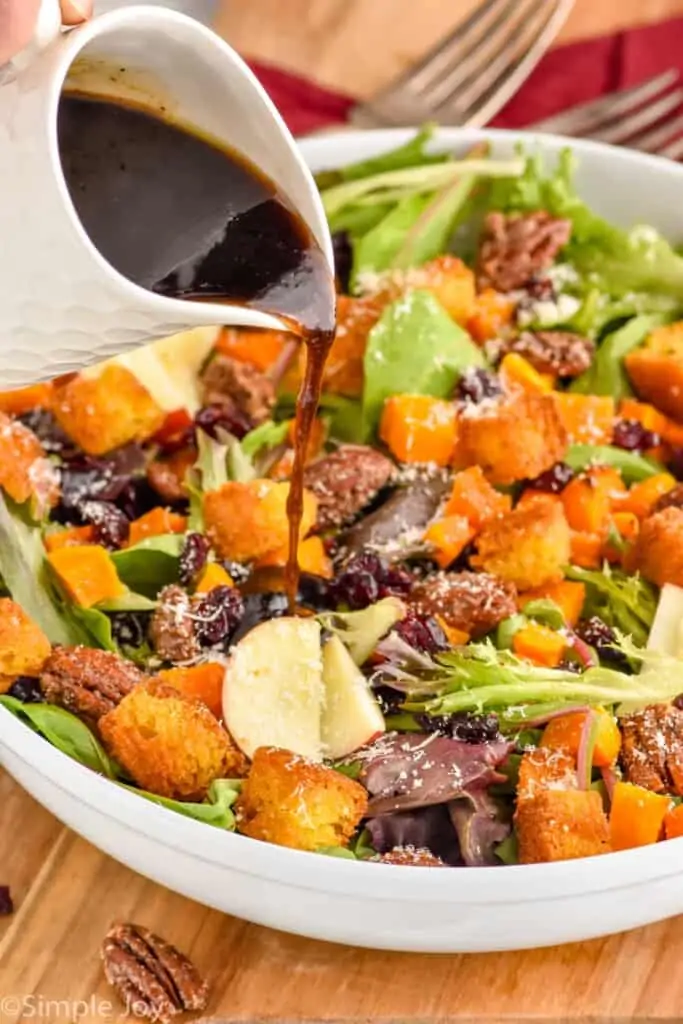 side view of a maple vinaigrette dressing being poured on a fall harvest salad