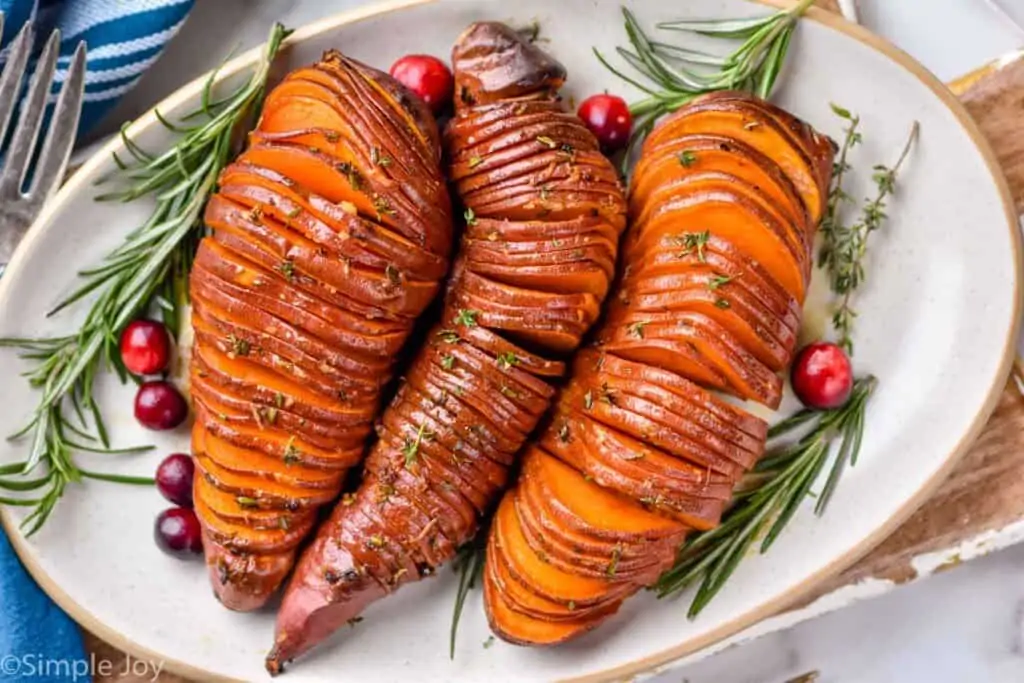 overhead of three hasselback sweet potatoes on a platter with fresh rosemary and cranberries