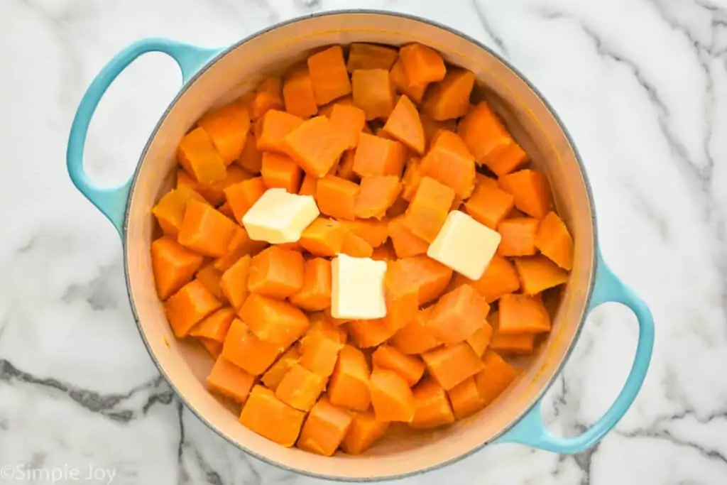 overhead of a dutch oven full of cooked cubed mashed sweet potatoes with three pads of butter