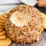 pinterest graphic of a cheese ball on a marble cutting board with a bit missing, surrounded by crackers and a cheese spreader in the background