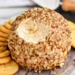 pinterest graphic of a cheese ball on a marble cutting board with a bit missing, surrounded by crackers and a cheese spreader in the background