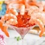 pinterest graphic of martini glass filled with shrimp cocktail sauce recipe and shrimp sticking out of it