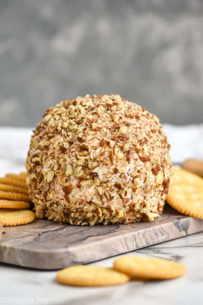 front picture of a cheese ball on a cutting board, coated in chopped pecans