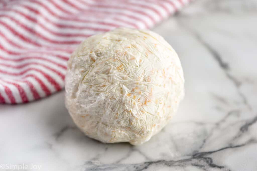 side view of a cheese ball wrapped in plastic wrap