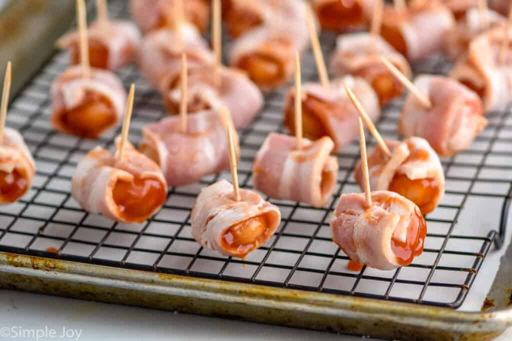 uncooked bacon wrapped water chestnuts on a cooling rack on top of a rimmed baking sheet lined with parchment paper