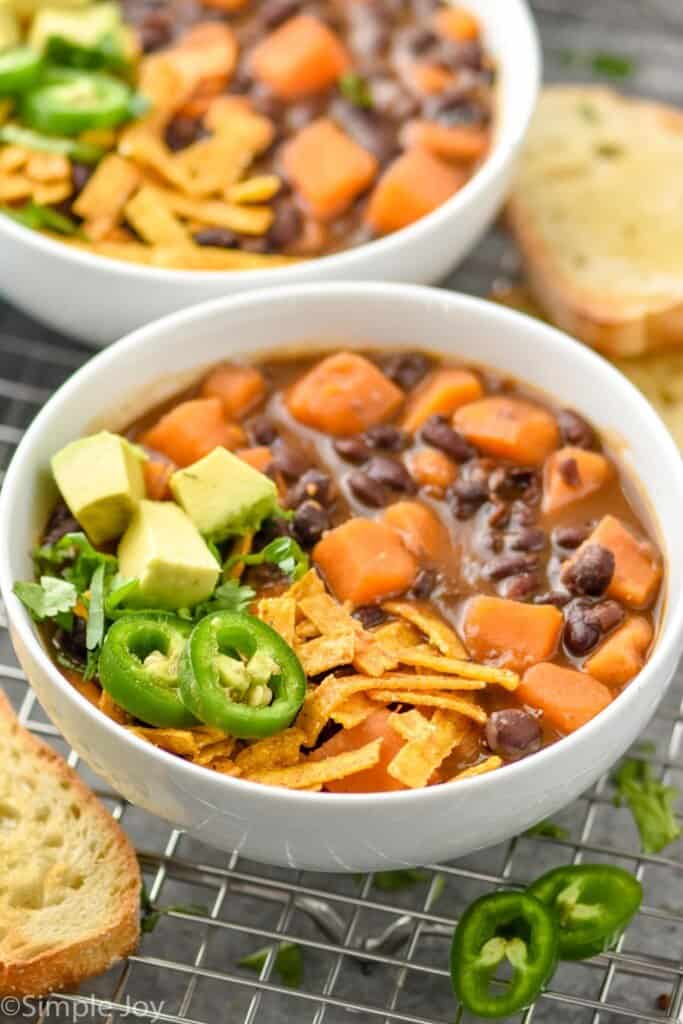 side view of a bowl of black bean soup recipe garnished with tortilla strips, fresh jalapeno slices, and avocado chunks