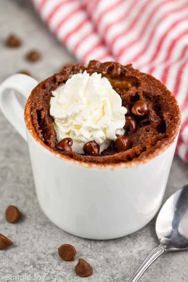 a small white mug with a chocolate mug cake in it, topped with whipped cream