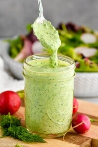 side view of a jar green goddess dressing with a spoon coming out