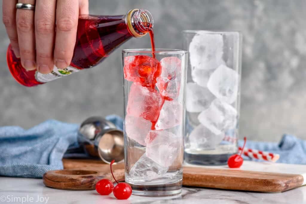 pouring grenadine into a glass filled with ice to make a Shirley Temple recipe